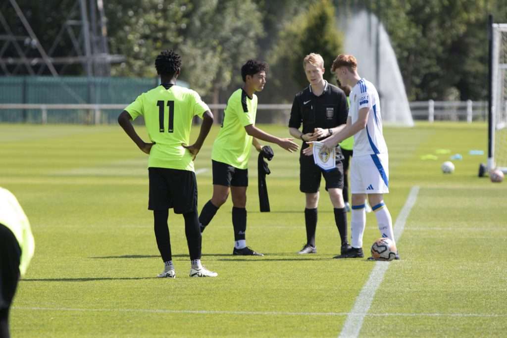 Players in lime green bibs and a referee during a UK football trial match