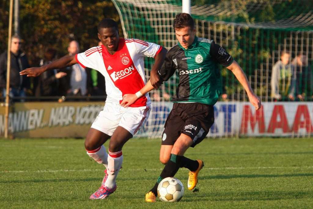 Player in a green and black kit challenging a player in red and white