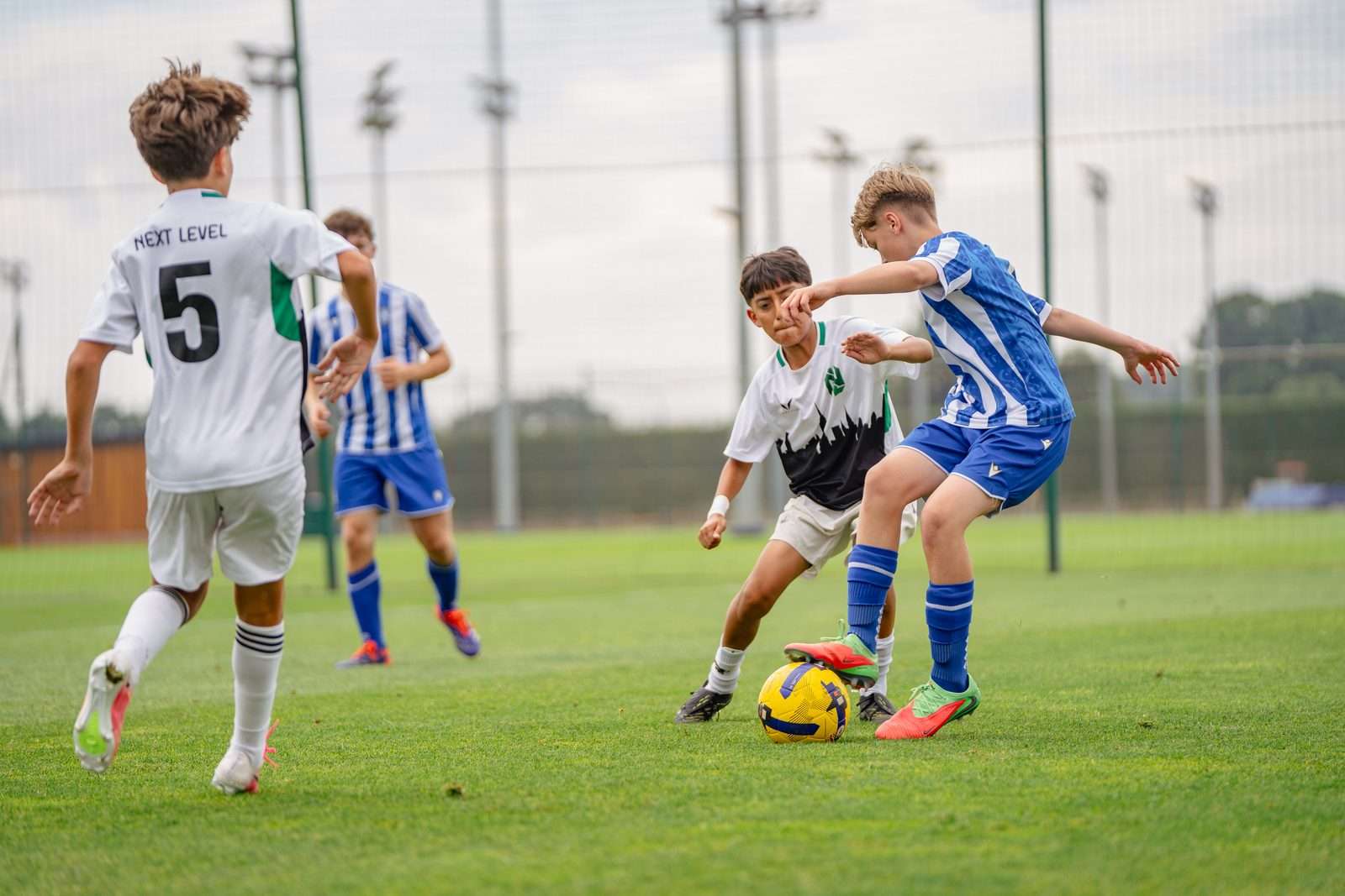Player in white tackles an opponent in blue and white stripes during a UK football trial match